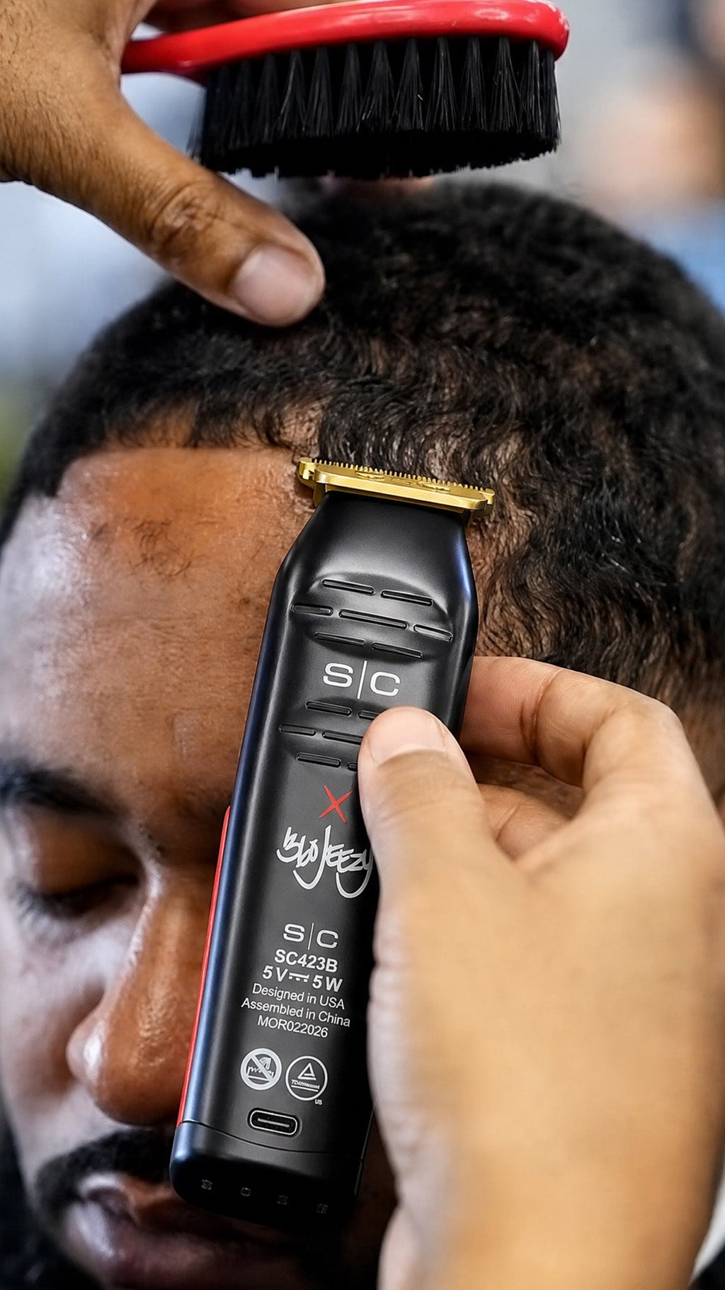 Cordless hair trimmer with gold blade and red-black body grooming a beard